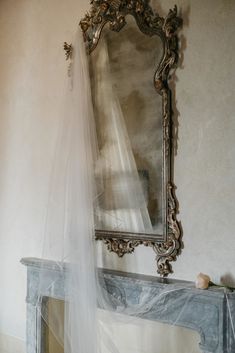 a white veil hanging over a fireplace with a mirror on the wall in front of it