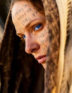 a woman with tattoos on her face is looking at the camera and has blue eyes