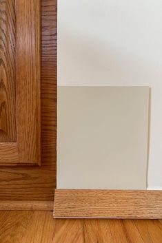 the corner of a room with wood flooring and white paint on the door frame