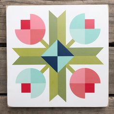 a white square with colorful geometric designs on the front and back of it, sitting on a wooden surface