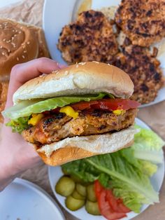 a person is holding a hamburger with lettuce and tomatoes