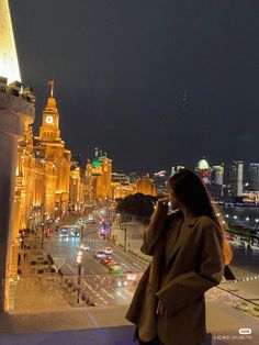 a woman standing on top of a balcony next to a tall building with a clock tower