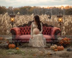 a pregnant woman sitting on a red couch in a field with pumpkins around her