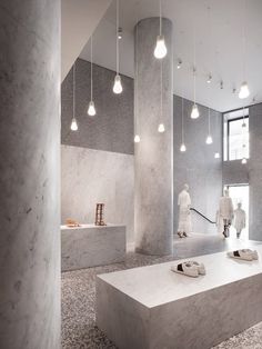 a room filled with lots of white and grey marble walls next to a staircase covered in hanging lights