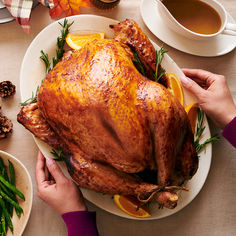 a person holding a turkey on a plate with oranges and green beans next to it