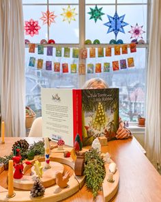 a child is sitting at a table with a book in front of them and christmas decorations on the window sill