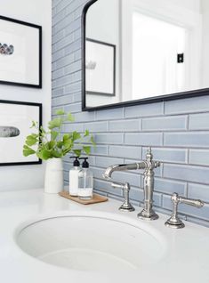 a white sink sitting under a bathroom mirror next to a vase with flowers on it