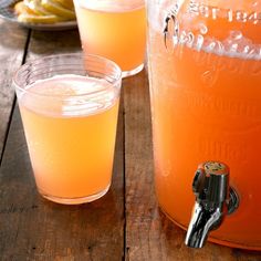 two glasses filled with orange liquid sitting on top of a wooden table next to a pitcher