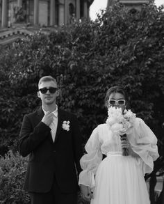 a man and woman standing next to each other in front of a building with trees