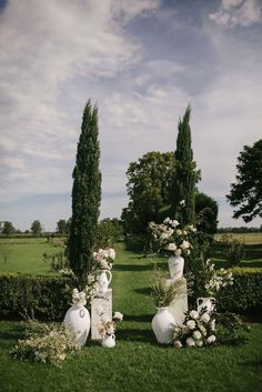 two white vases sitting in the middle of a lush green field