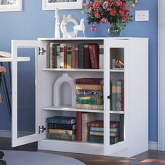 a white bookcase with books and flowers on top in a blue walled living room