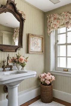 a white sink sitting under a mirror in a bathroom next to a window with flowers on it