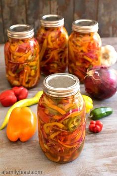 several jars filled with pickles and peppers sitting on a table next to other vegetables