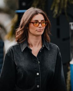 a woman wearing sunglasses and a black shirt is walking down the street with her hands in her pockets