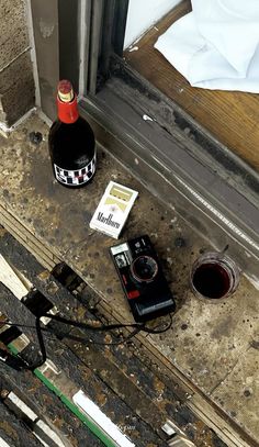 a bottle of wine sitting on the ground next to a cell phone and some papers