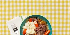 a blue bowl filled with meat and vegetables next to a fork on a yellow checkered table cloth