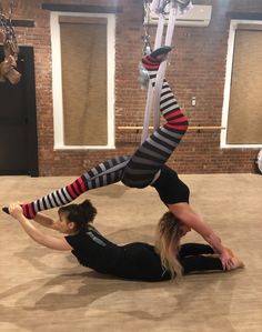 two women doing aerial acrobatic exercises in a dance studio