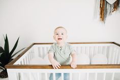 a baby standing in a crib with his hands on the rail and looking at the camera