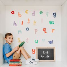 a young boy sitting on top of a book shelf next to a blackboard with colorful letters