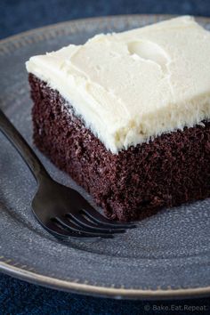 a piece of chocolate cake with white frosting on a plate next to a fork