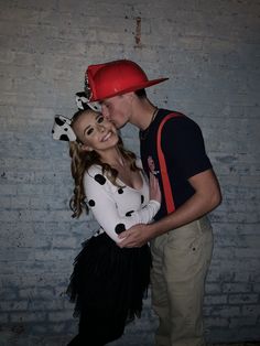 a man and woman dressed in costumes posing for a photo with a brick wall behind them