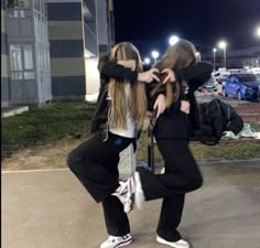 two young women standing next to each other in front of a parking lot at night