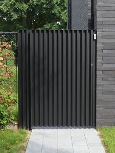 a black gate is in front of a brick wall and green grass on the other side