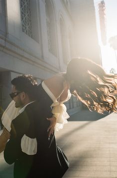 a man and woman are walking down the street in front of a building with their arms around each other