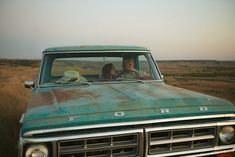 two people sitting in the front seat of an old pickup truck on a dirt road