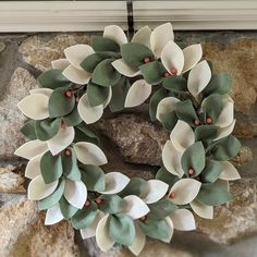 a wreath with white and green leaves hanging on a stone wall