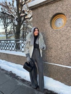 a woman standing next to a building in the snow with her hand on her hip