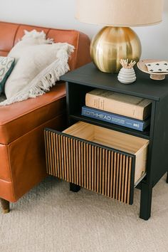 a brown couch sitting next to a black table with books on it and a lamp