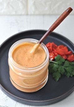 a jar of sauce on a black plate next to red peppers and cilantro