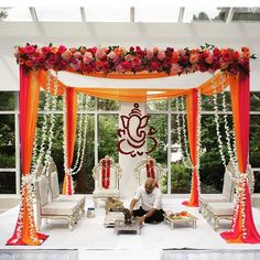 a man sitting in front of a white and orange stage set up with flowers on it