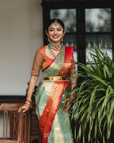 a woman in a green and red sari standing next to a plant with her hands on the ground