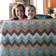 an older woman and young boy holding up a crocheted blanket