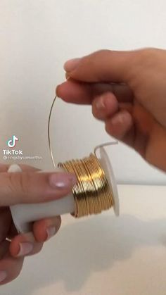 two hands are holding some gold wire and one hand is pulling on the end of it