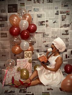 a woman is sitting on the floor with balloons and books in her hand while drinking from a mug