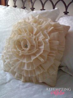 a white pillow with a flower on it sitting on a bed in front of a headboard