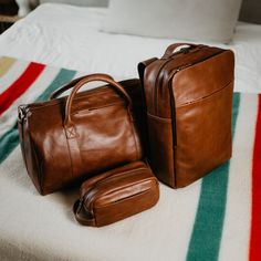 two brown leather bags sitting on top of a bed