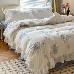 the bed is made with white linens and blue flowers on it, along with two pillows