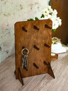 there is a wooden key holder with keys in it on the table next to flowers