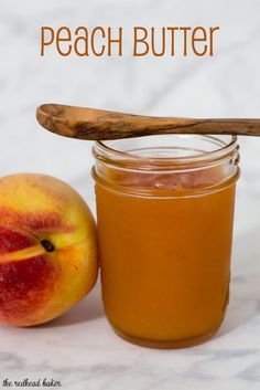 a jar of peach butter next to an apple on a table with a wooden spoon