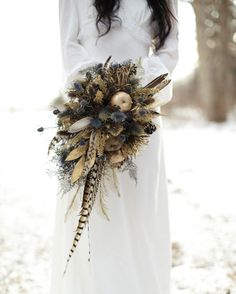 a woman in a white dress holding a bouquet with feathers and other things on it