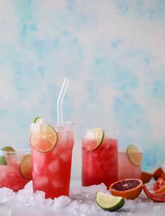 three glasses filled with watermelon and limeade on ice next to sliced oranges