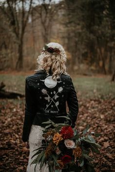 a woman standing in the woods with her back to the camera holding a bouquet of flowers