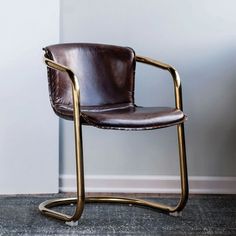 a brown leather chair sitting in front of a white wall with a gold metal frame