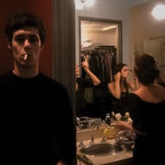 a man standing in front of a bathroom mirror with his mouth open and two women brushing their teeth