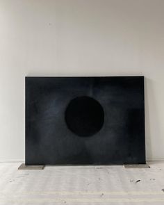 a black square sculpture sitting on top of a white floor in front of a wall