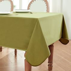 a green table cloth on top of a wooden dining room table with white plates and silverware